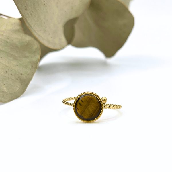 Bague délicate en acier inoxydable doré avec pierre marron, posée sur un fond végétal.