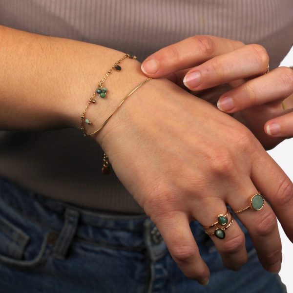 Bras portant un bracelet doré avec des pierres vertes et deux bagues en acier inoxydable.