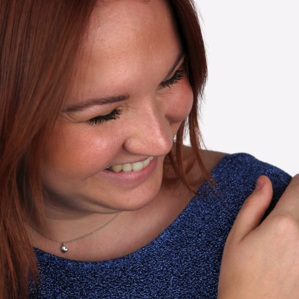 Femme souriante avec un collier argenté avec un pendentif en forme de coeur